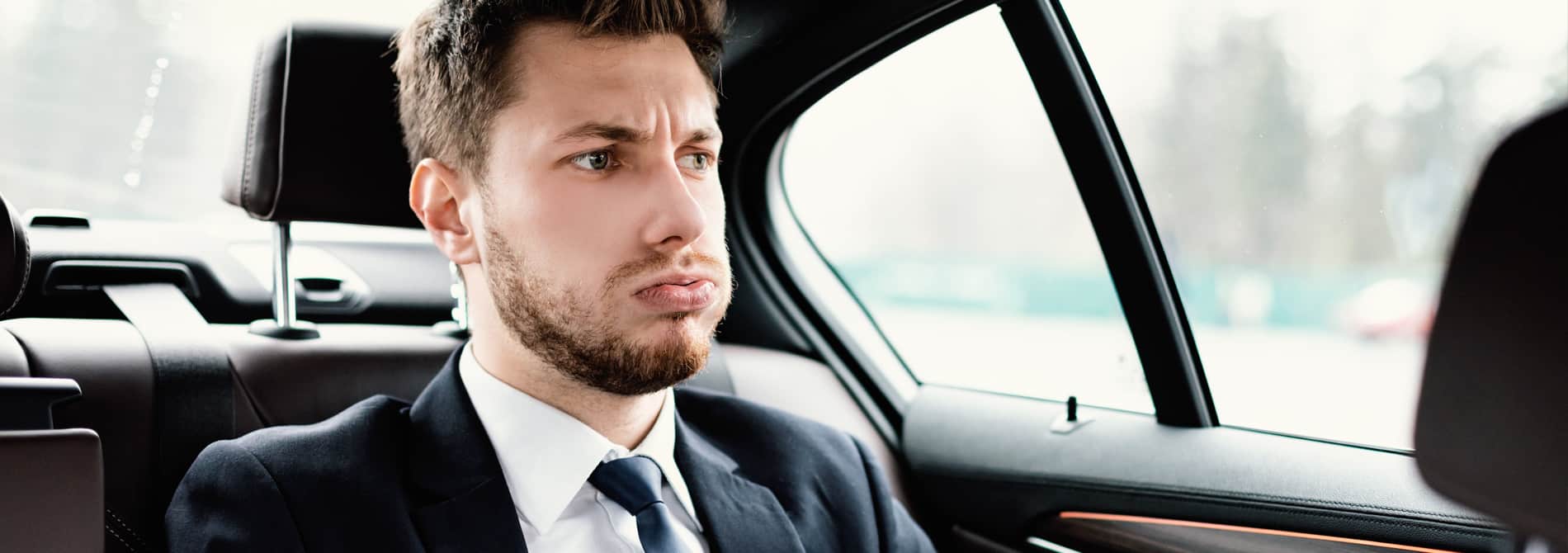 Young wealthy man stressed out in back of car.